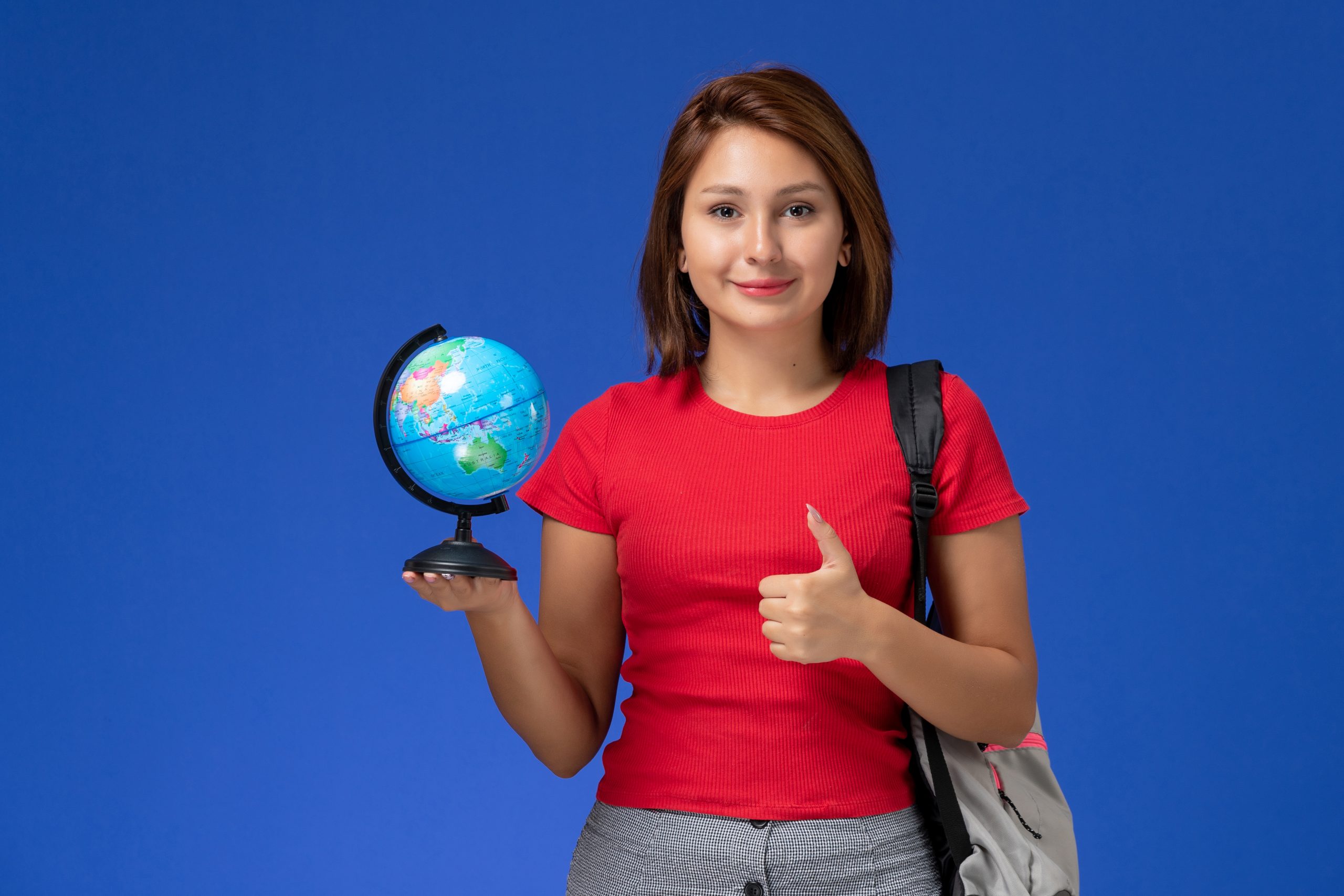 front-view-female-student-red-shirt-with-backpack-holding-little-globe-smiling-blue-wall